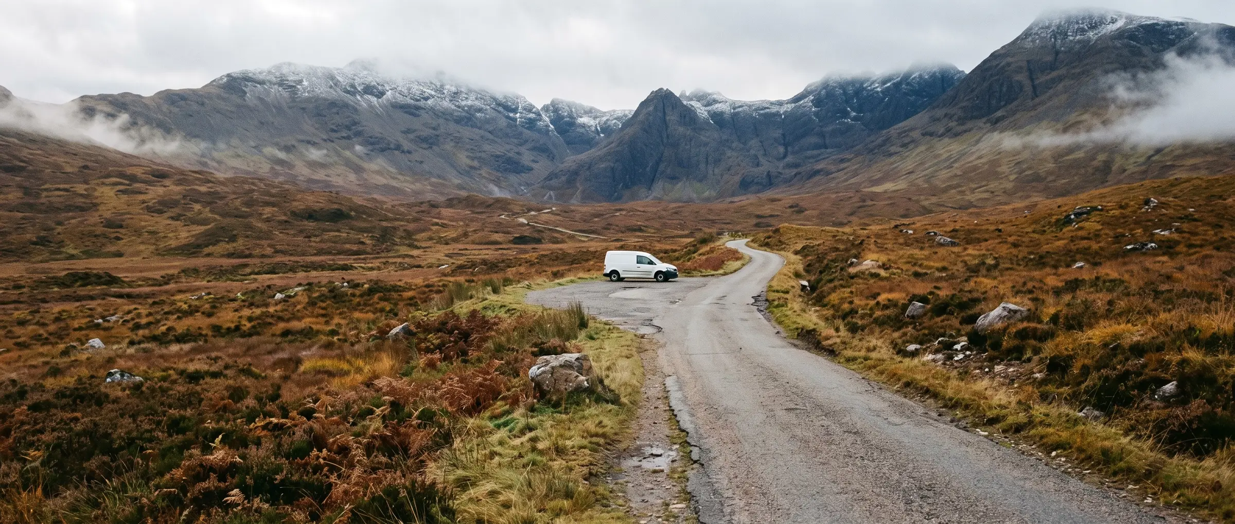 A single-track road through a Highland glen towards snow-dusted mountains, with a work van in a passing place